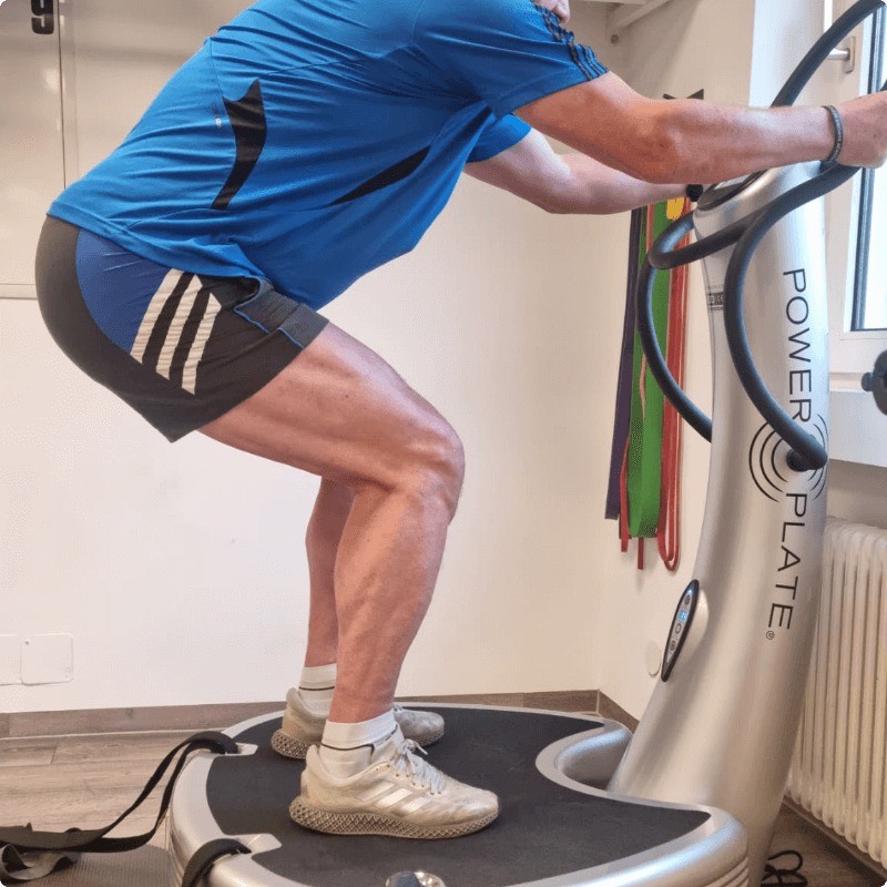 Trainierender in der Kniebeuge auf einer Power Plate, die Hände am Haltebügel des Geräts