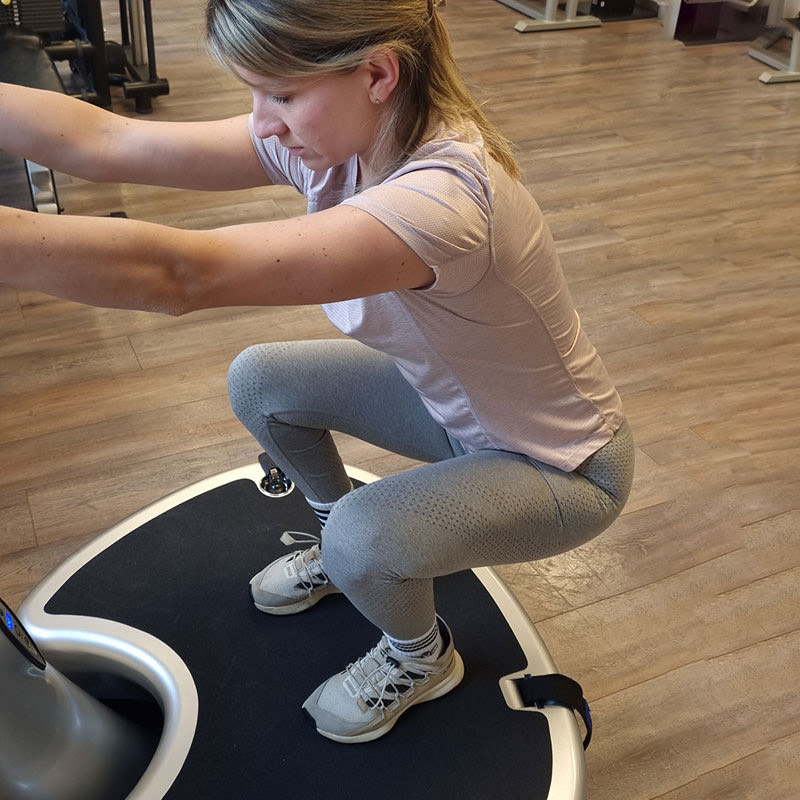 Trainierende in der tiefen Hocke auf einer Power Plate im Trainingsbereich von AS Physio