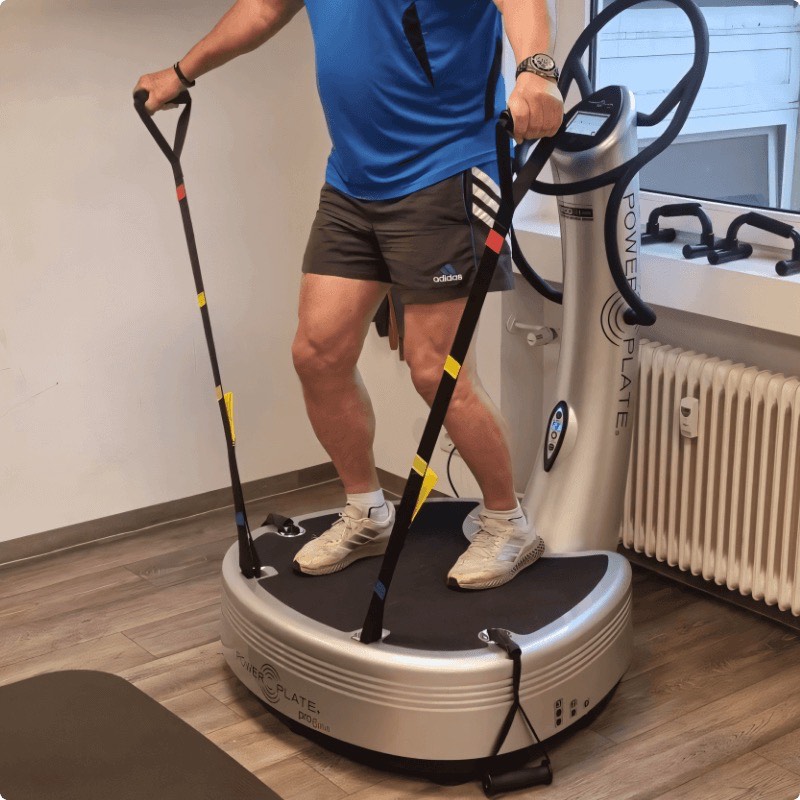 Training mit Zugbändern im Stand auf einer Power Plate im Trainingsraum von AS Physio